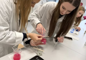 Dwie uczennice pochylone nad stabilizacją knota w świecy