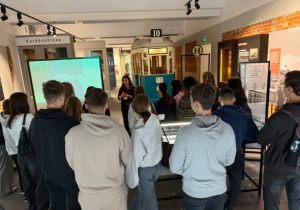 Uczniowie w sali muzealnej na tle tramwaju linii 10