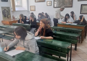 Uczniowie w zielonych ławkach piszący notatki