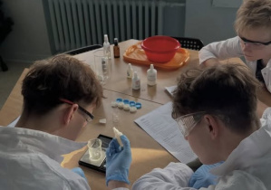 3 uczniów przy stole w okularach ochronnych podczas doświadczeń