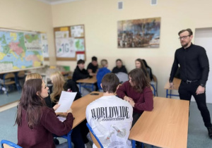 Uczniowie w grupach przy ławkach ze stojącym radcą