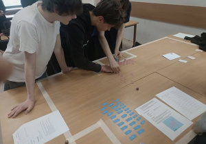 Uczniowie pochyleni nad stołem z quizem do rozwiązania