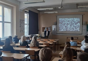 Uczniowie w sali wykładowej z ekranem siedzący tyłem do fotografa